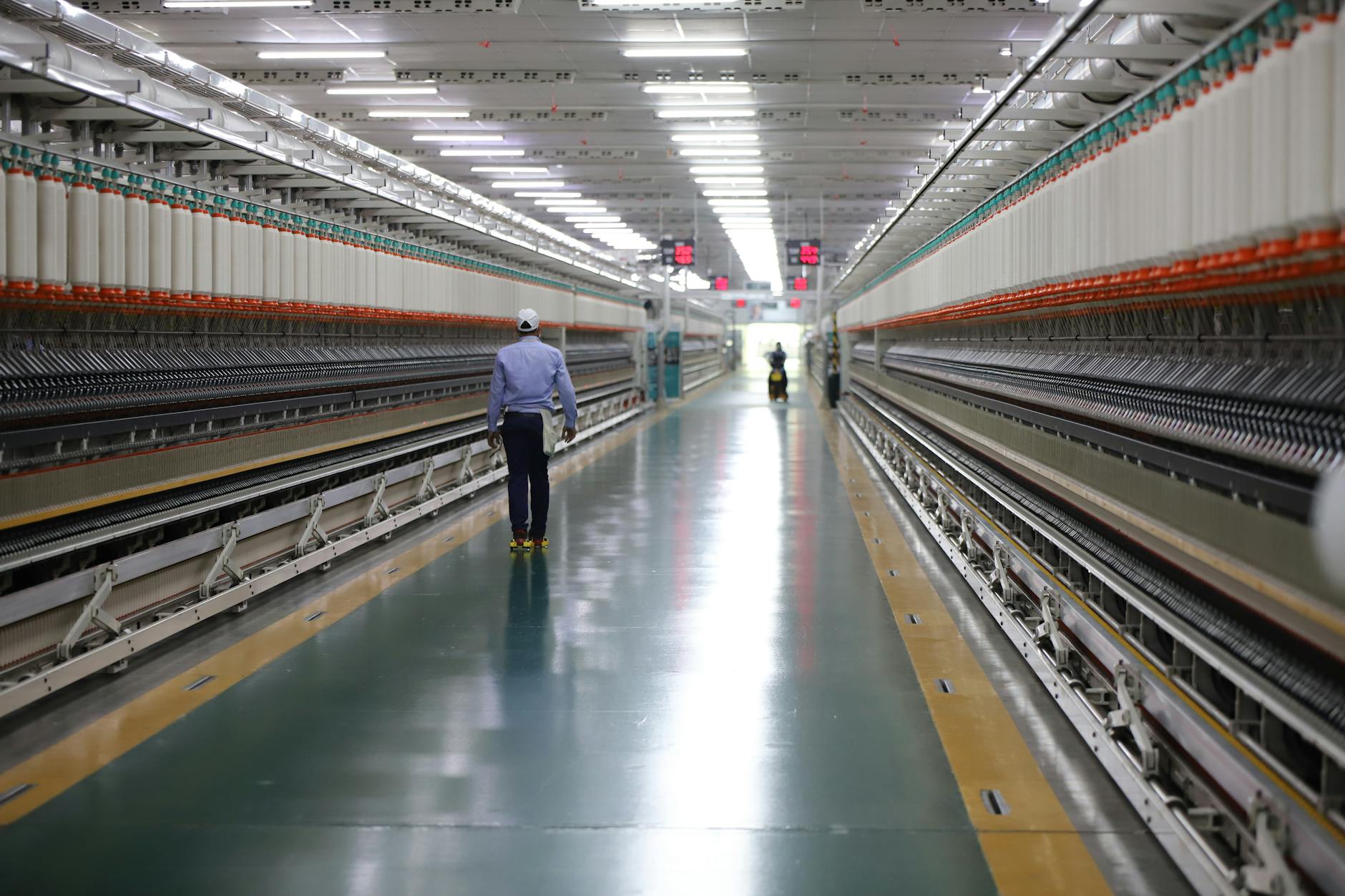 A Man in Blue Long Sleeves Walking Beside the Industrial Machinery