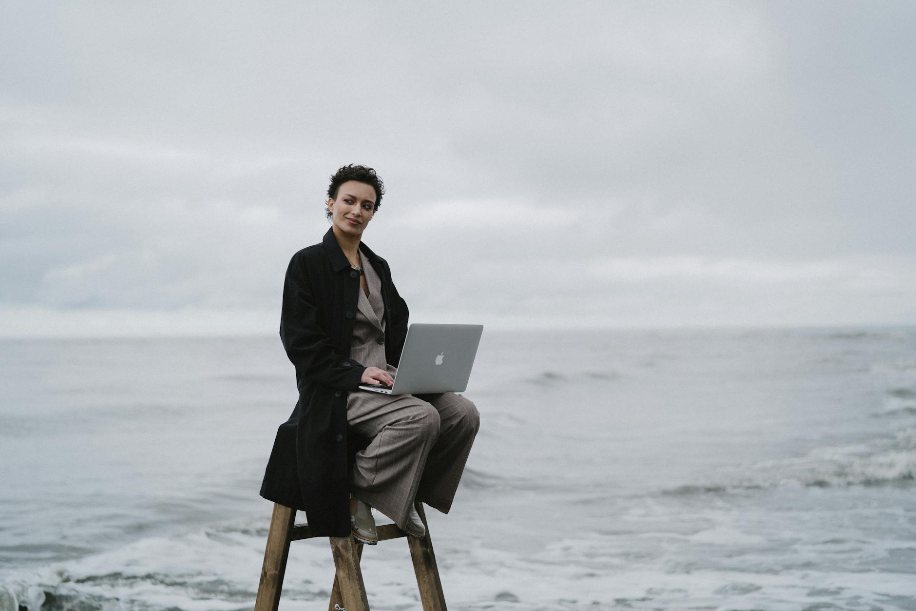 A person with a laptop sitting on a ladder by the ocean, symbolizing remote work.